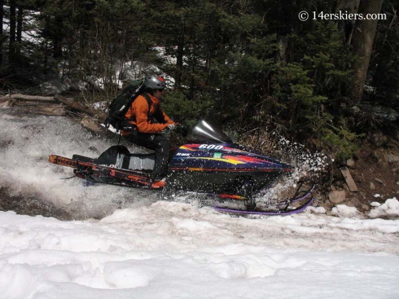 Frank Konsella snowmobiling across a stream. 